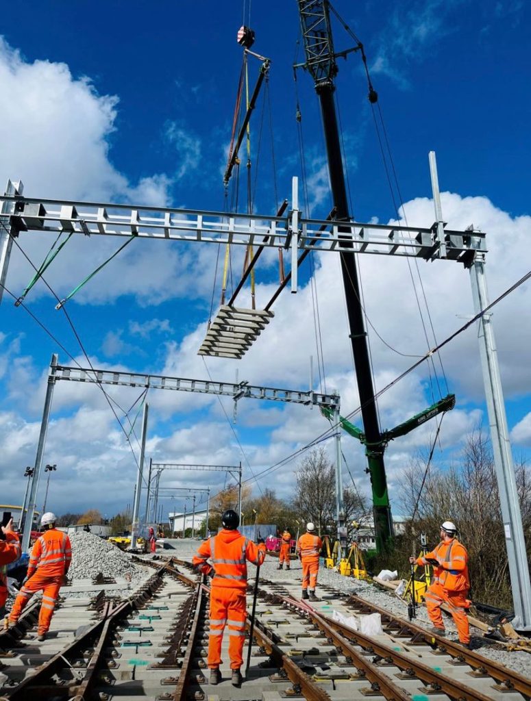 King Lifting crane technicians installing railway overhead electrical infrastructure, wearing high-visibility orange safety gear